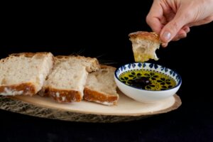 Šviežia duona šalia dubenėlio su auksiniu alyvuogių aliejumi ant medinio stalo.